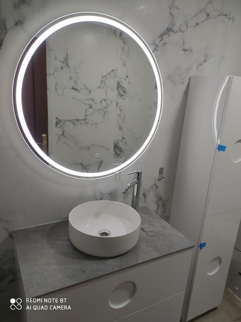 Baño en obra con espejo circular retroiluminado y lavabo sobre encimera