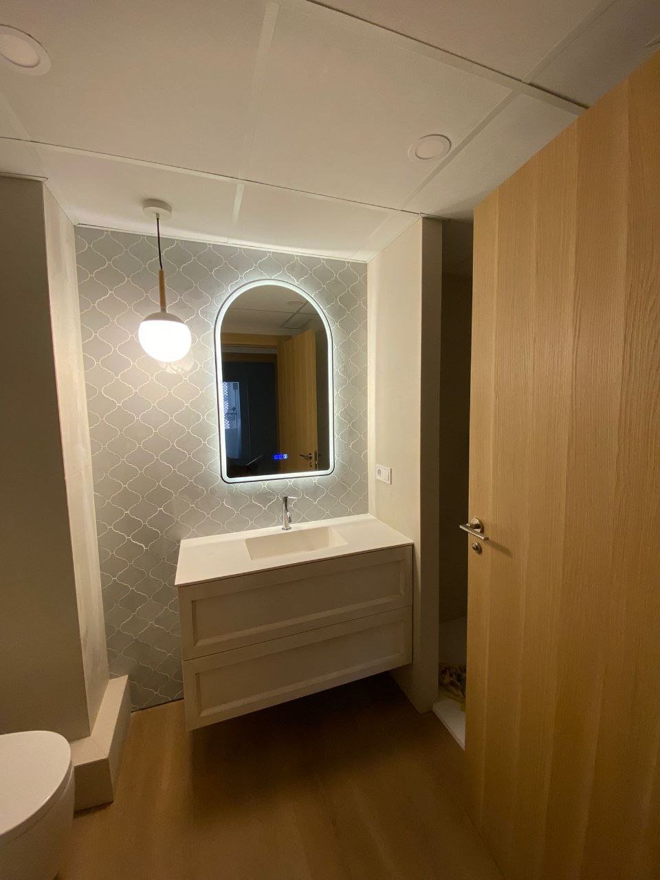Baño reformado con azulejo tipo escama, espejo retroiluminado y lámpara colgante