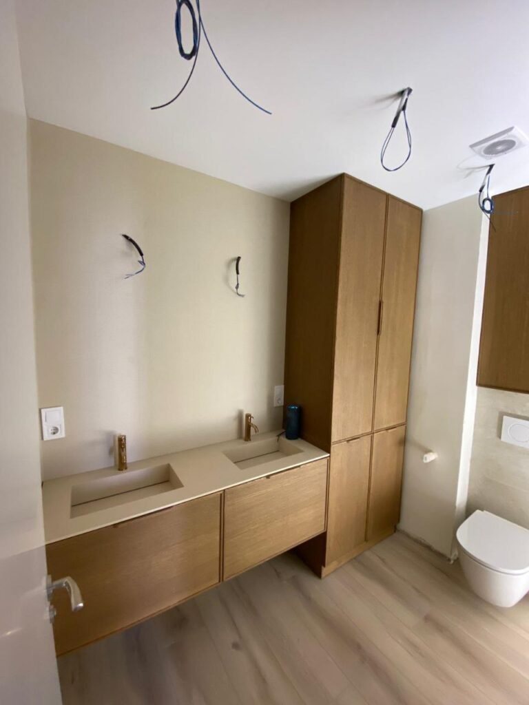 Baño reformado con doble seno, armario columna de madera e inodoro suspendido