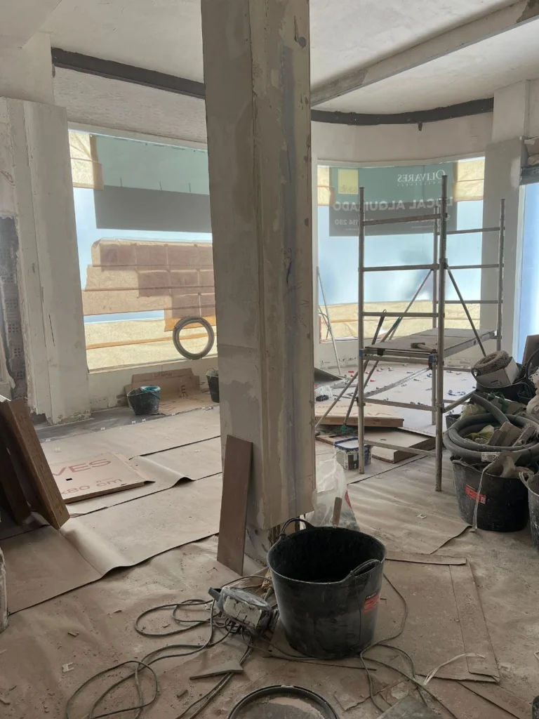 Local diáfano en obra con pilar central, andamio y protección de suelo