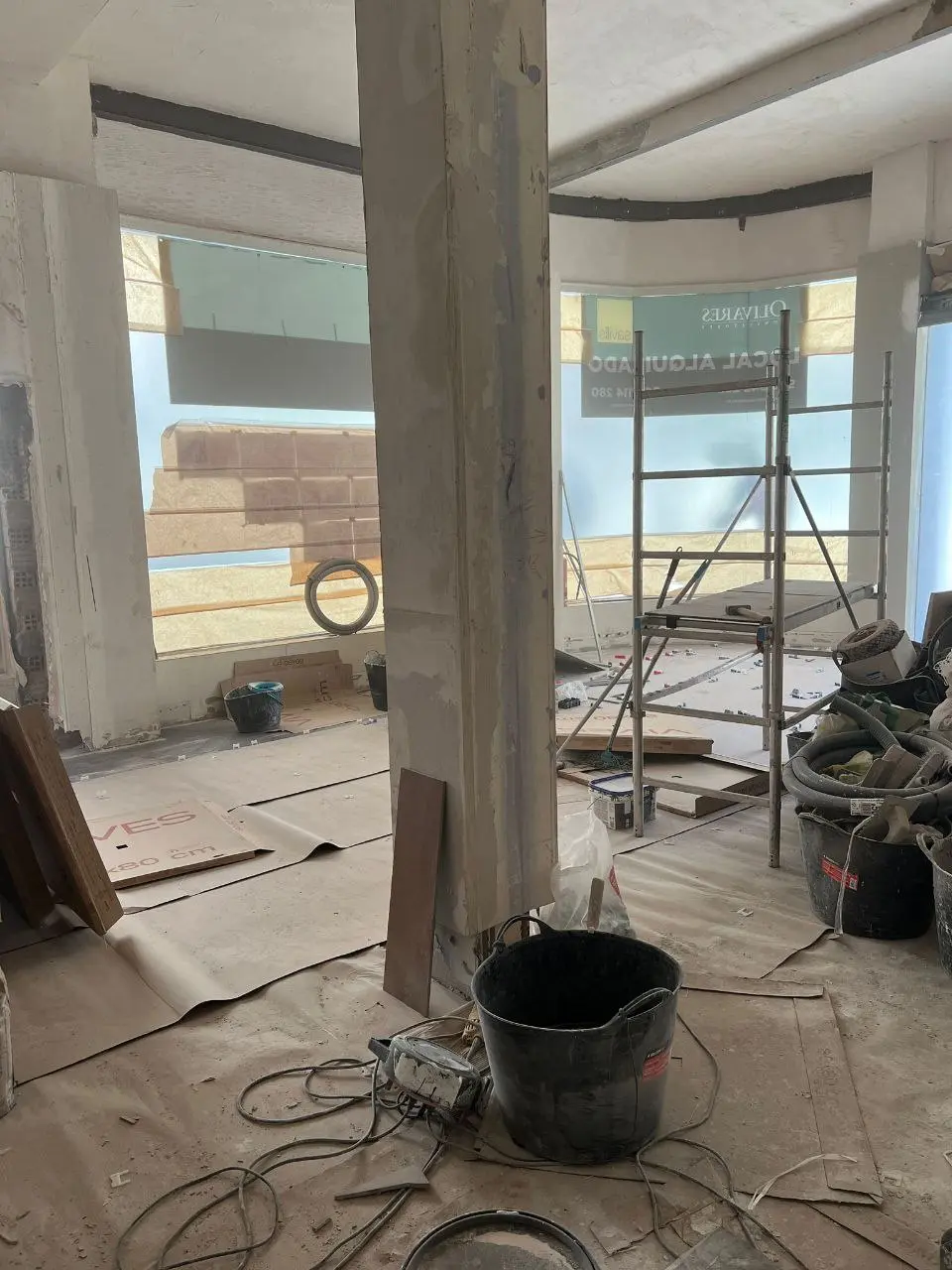 Local diáfano en obra con pilar central, andamio y protección de suelo