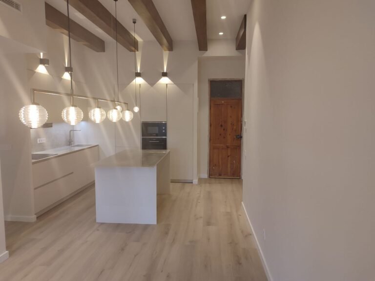 Cocina abierta reformada con isla central, iluminación colgante y vigas vistas