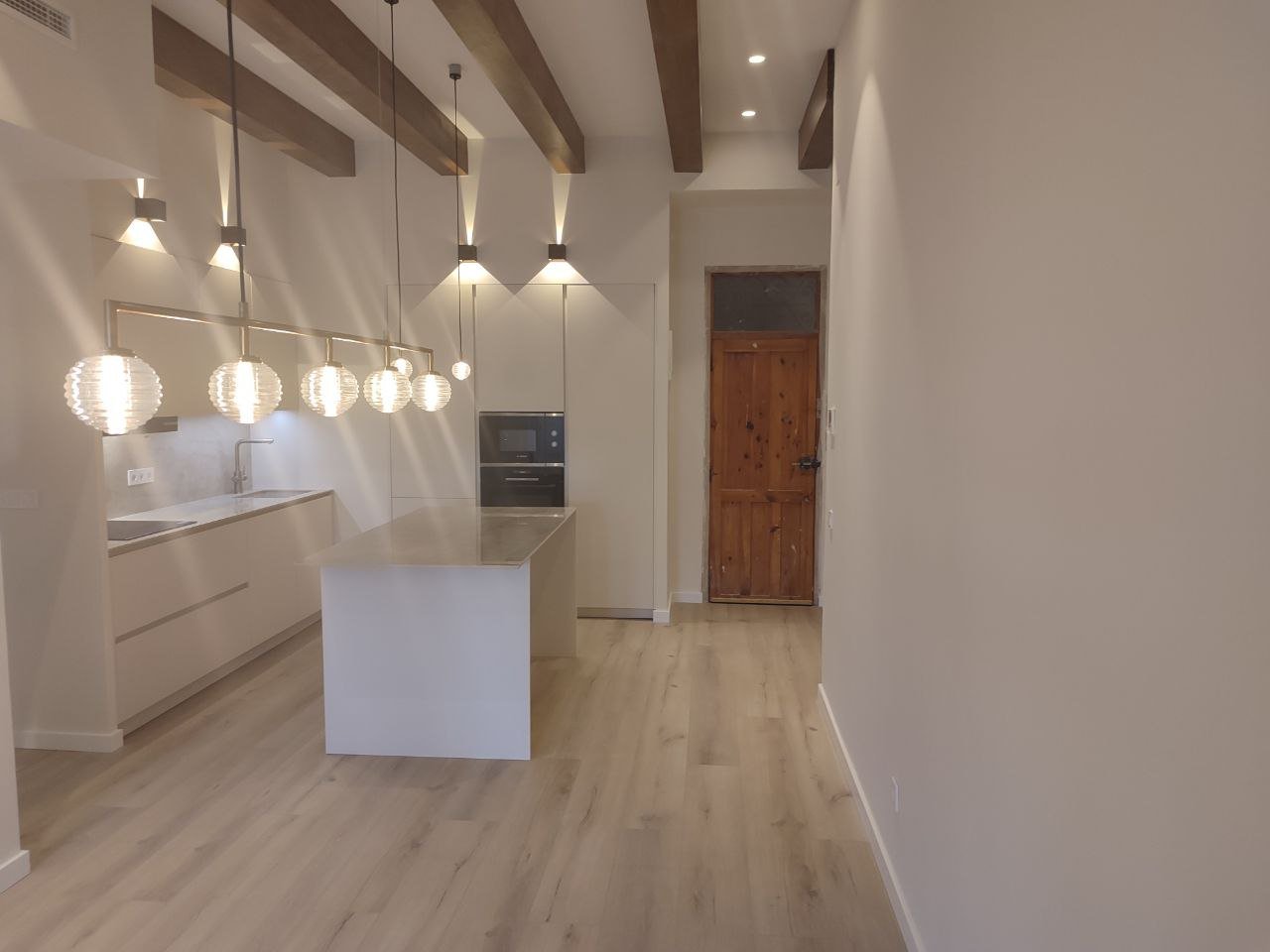 Cocina abierta reformada con isla central, iluminación colgante y vigas vistas
