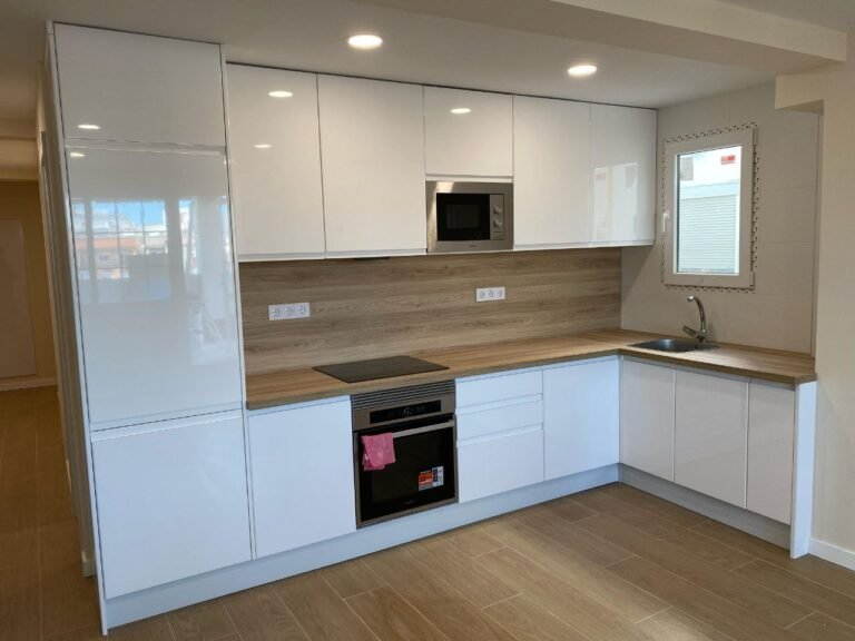 Cocina blanca reformada con encimera de madera, placa de inducción y fregadero bajo ventana